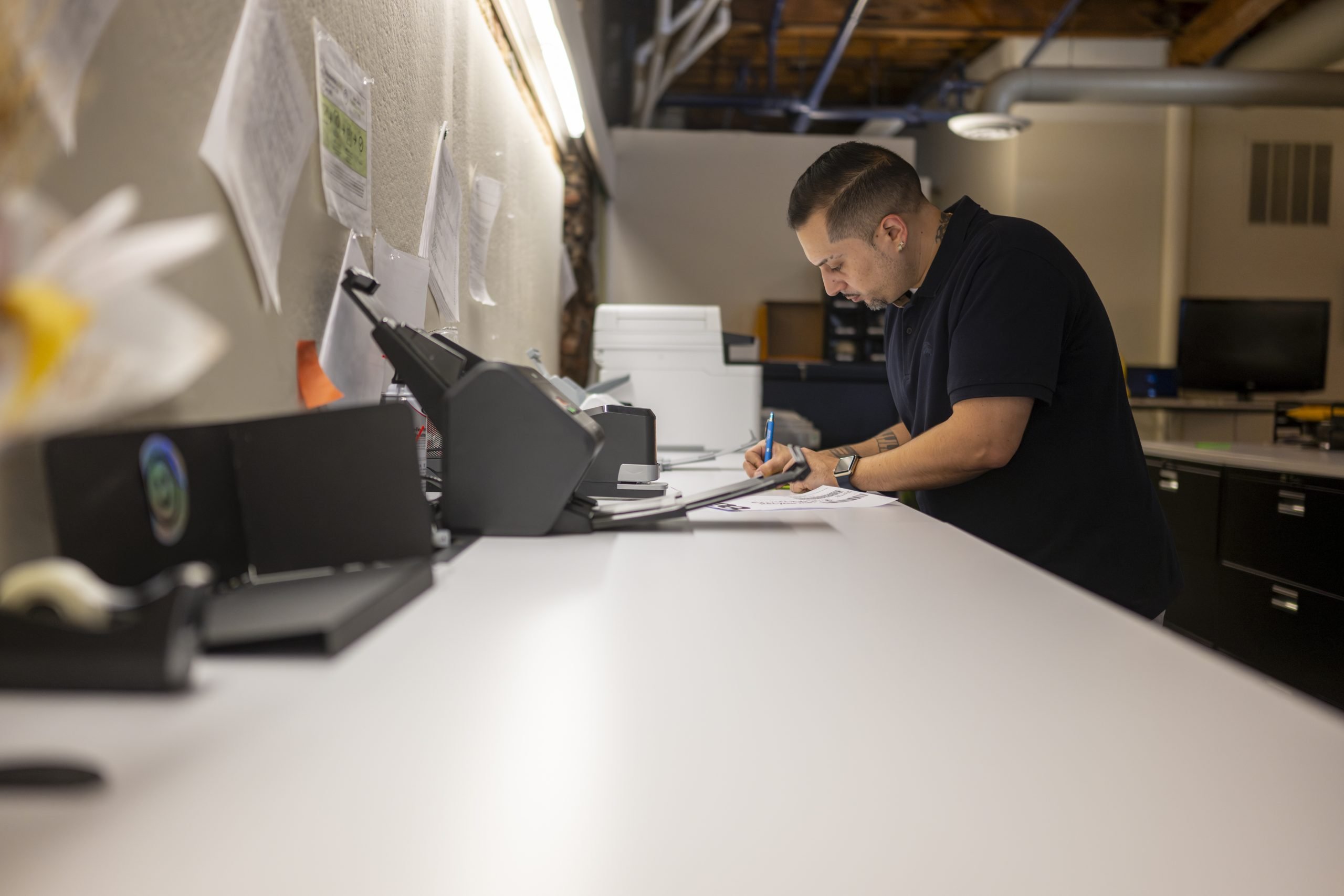 A male employee of New York Registered Agent signing paperwork on along desk.